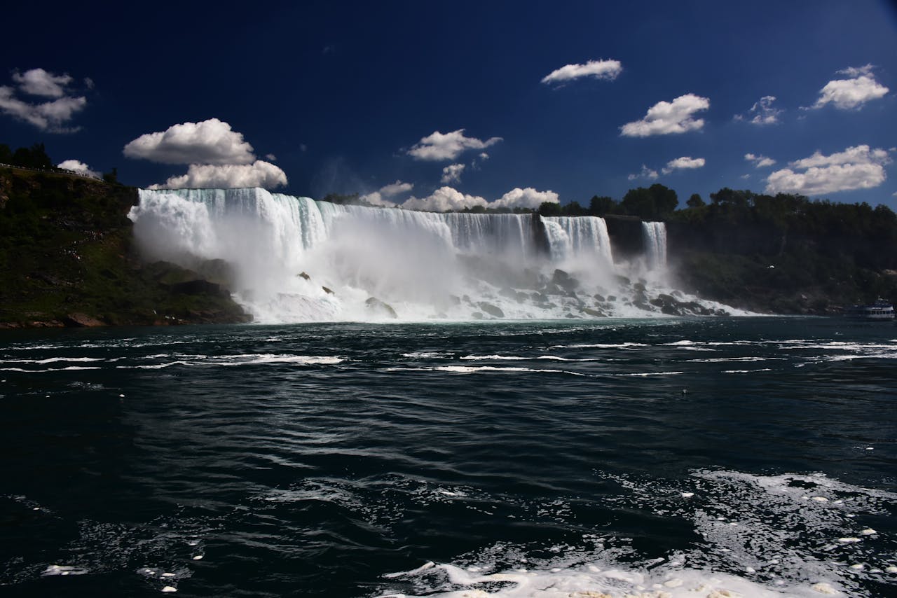 Stunning view of Niagara Falls with cascading water under a bright blue sky and fluffy clouds.